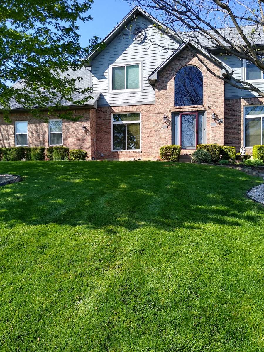 A brick and blue-siding two-story house with a freshly mown, green front lawn and trimmed shrubs along the foundation.
